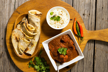 Close-up of flatbread with meat gravy and rice in bowls with cilantro and chili on serving board