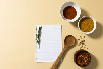  Directly above shot of spices in bowls with notepad and rosemary on beige background, copy space © vectorfusionart