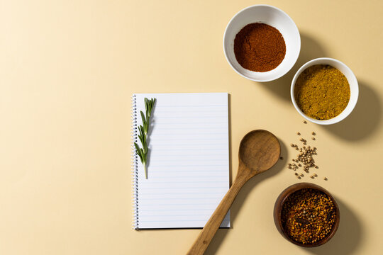 Directly above shot of spices in bowls with notepad and rosemary on beige background, copy space