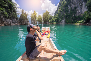 An asian man stands arms up while on a wooden boat in the middle of the water happily on holiday.