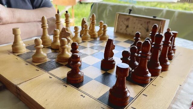 Chess game board closeup. Senior men hand moving figure in strategy game. Closeup unknown old men arms playing chess alone indoors. Unrecognizable man playing smart game tactic. Business strategy