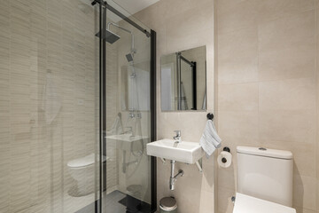 Stylish comfortable bathroom with a glass-enclosed shower, toilet and sink and a mirror in light colors with beige tiles. The concept of a comfortable hotel room with a modern interior