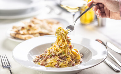 A person's hand takes spaghetti carbonara out of a plate in a restaurant