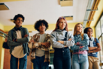 Group of happy teenagers standing with their arms crossed at high school and looking away.
