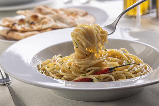 Spaghetti aglio e olio spinned on a fork taking a mouthful portion of pasta out of the plate