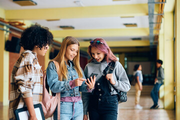 Group of high school students using cell phone in hallway.