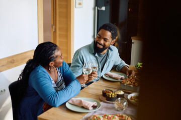 Fototapeta premium Happy black couple toasting with wine while eating at dining table.