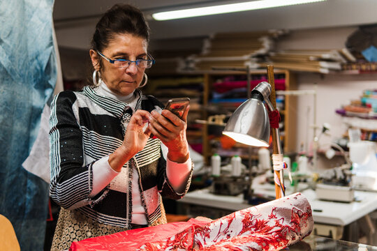 working seamstress looking on the smartphone in her sewing workshop - Powered by Adobe