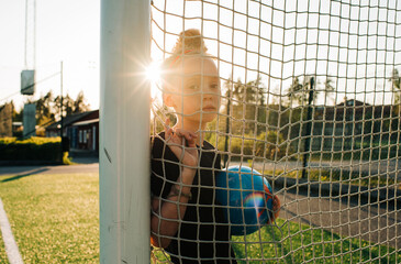 girl leaning against a goal post looking through a net at sunset