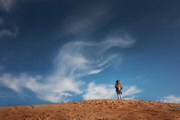 Young girl standing on a hill looking at blue sky with clouds