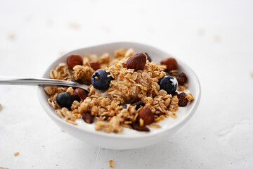 yogurt with granola, nuts and blueberries close-up in a round plate with a spoon. healthy breakfast rich in minerals and fiber