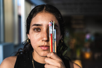 Close up of creative woman with color brush covering one eye.