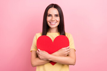 Photo of pretty adorable woman dressed yellow t-shirt smiling embracing red heart isolated pink color background