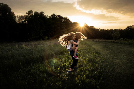 Young girls twirling in grassy field at sunset