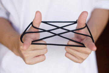 Closeup boy hands is playing rope which called cats cradle game. Concept, game involving the creation of various style figures between the fingers. Traditonal playing.    