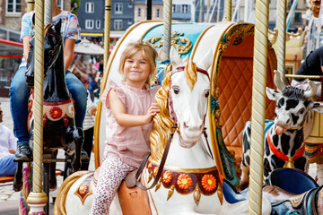 Adorable little girl and school kid boy having a ride on the old vintage merry-go-round in city of...
