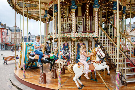 Adorable little girl and school kid boy having a ride on the old vintage merry-go-round in city of Honfleur France. Siblings, brother and small sister having fun.