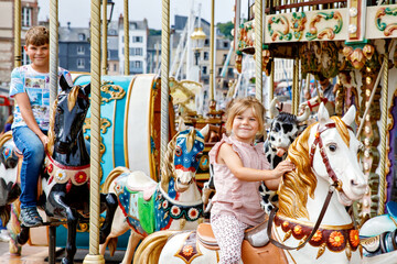 Fototapeta na wymiar Adorable little girl and school kid boy having a ride on the old vintage merry-go-round in city of Honfleur France. Siblings, brother and small sister having fun.
