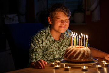 Happy blond little kid boy celebrating his birthday. Preteen child blowing candles on homemade baked cake, indoor. Birthday party for school children, family celebration