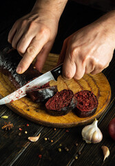 The chef cuts blood sausage on a kitchen cutting board with a knife. Cooking a national dish with spices and garlic in the kitchen
