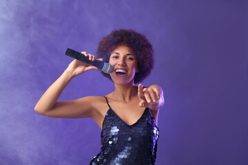Curly young woman with microphone singing on purple background