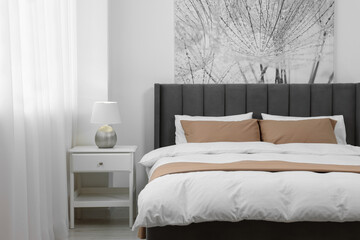 Comfortable bed and lamp on bedside table in light room. Stylish interior