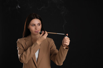 Obraz premium Woman using long cigarette holder for smoking on black background, space for text