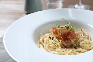 Tasty spaghetti with prosciutto and microgreens on plate, closeup. Exquisite presentation of pasta dish
