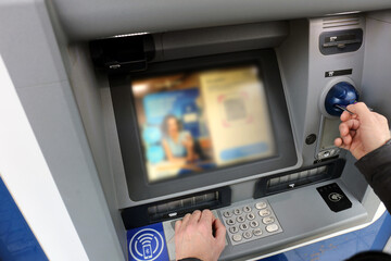 A male customer making a transaction with a credit card or debit card at an ATM Automated Teller Machine