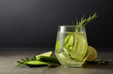 Cocktail gin tonic with ice, rosemary, lime, and cucumber on a stone table.