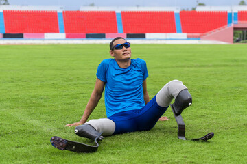 Asian paralympic athlete, poised on the grass lawn with his prosthetic running blades, patiently...