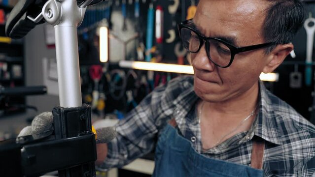 Expert senior man tightening the screw and checking bike handlebars in cycle store. Happy senior repairman maintenance bicycle in bike shop. Maintenance and repair concept