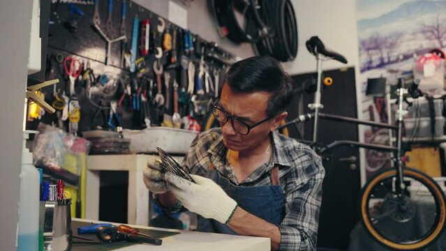 Professional senior Asian man tightening the screw gear of bike in cycle store. Senior repairman fixing cog of bike wheel on table in bicycle shop. Maintenance and repair concept