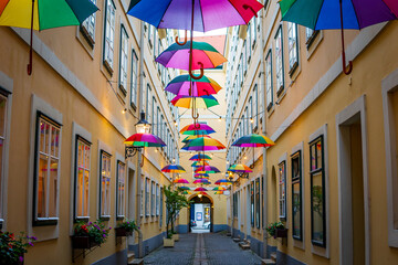 Fototapeta premium Colorful umbrellas decorating a narrow street, between old European yellow buildings. Colored umbrellas sky making a festive, fun, setting in Vienna, Austria. Happy, colorful, and pride concept.