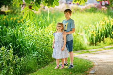 Fototapeta premium School kid boy and little sister, preschool girl playing together in park. Two happy children play and having fun sunny summer day. Siblings in love. Lovely sister and brother.