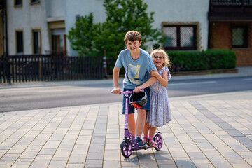 Preschool girl and school boy riding scooter in the city. Little sister and kid brother ride a...