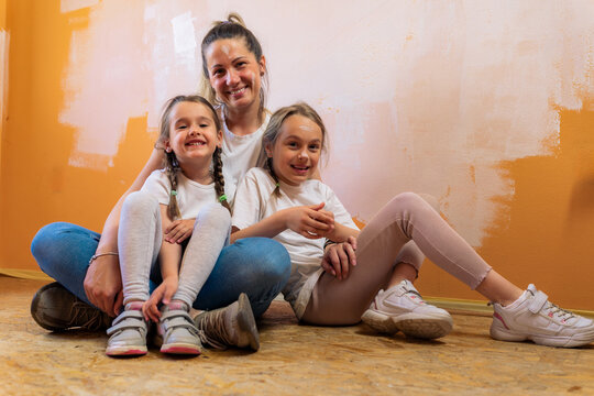 A mother hugs her daughters as they sit on the floor of the room they are renovating