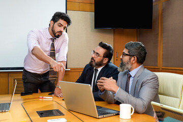 Young indian ceo presenting project information to other businesspeople, using laptop and white board.