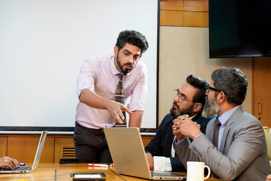 Young indian manager presenting project information to other businesspeople, using laptop and white board.