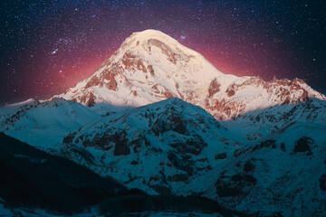 Georgia. Winter Bold Bright Night Starry Violet Gradient Sky With Glowing Stars Over Peak Of Mount Kazbek Covered With Snow. Amazing Night Georgian Winter Landscape. Travel To Georgia.
