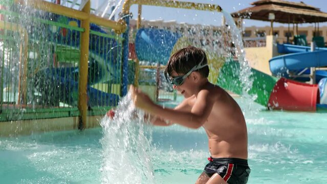 Overjoyed male kid splashing water aqua park swimming pool jumping happy childhood slow motion
