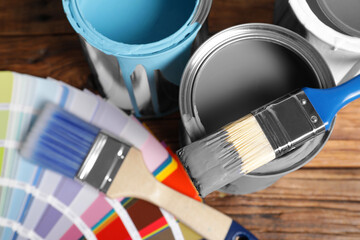 Cans of paints, brushes and color palette on wooden table, closeup