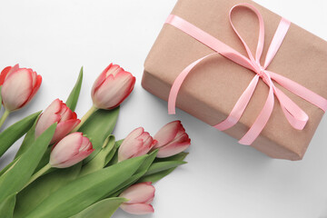 Beautiful gift box with bow and pink tulips on white background, flat lay