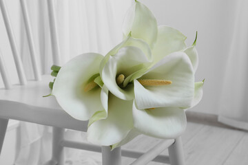 Beautiful calla lily flowers on white chair indoors, closeup