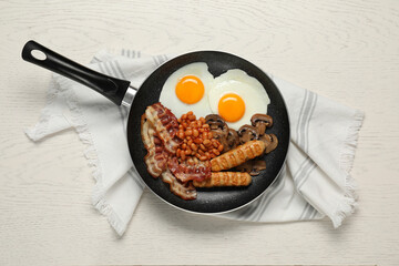 Frying pan with cooked traditional English breakfast and napkin on white wooden table, top view