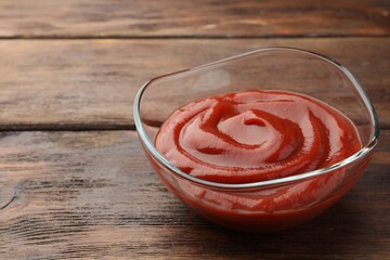 Bowl of tasty ketchup on wooden table, closeup. Space for text