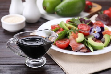 Tasty soy sauce and plate with salad on wooden table, selective focus
