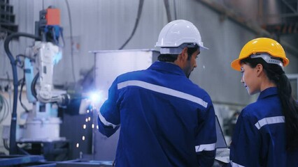 Two professional engineers control manage robot arm welding automation in heavy industry. Man and woman working by welding robot together in steel factory. Manufacturing automatic system concept