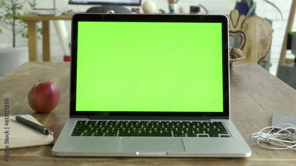 Poster Laptop is placed on wooden table and camera is in front of it (POV). Laptop display is with green screen ready for making a mock up.