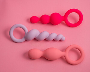 A set of three silicone anal beads of various shapes and sizes on an pink background.